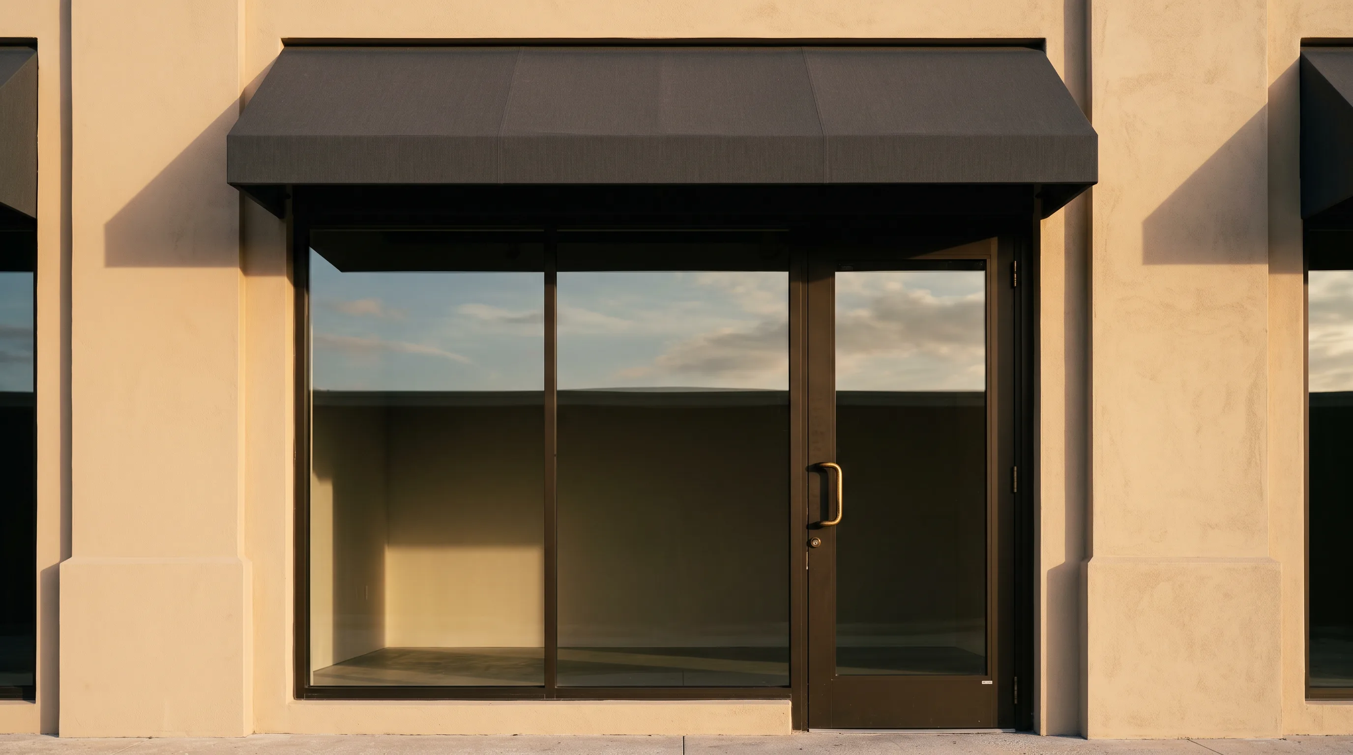 Retail storefront bay under a plain awning, its glass holding evening cloud