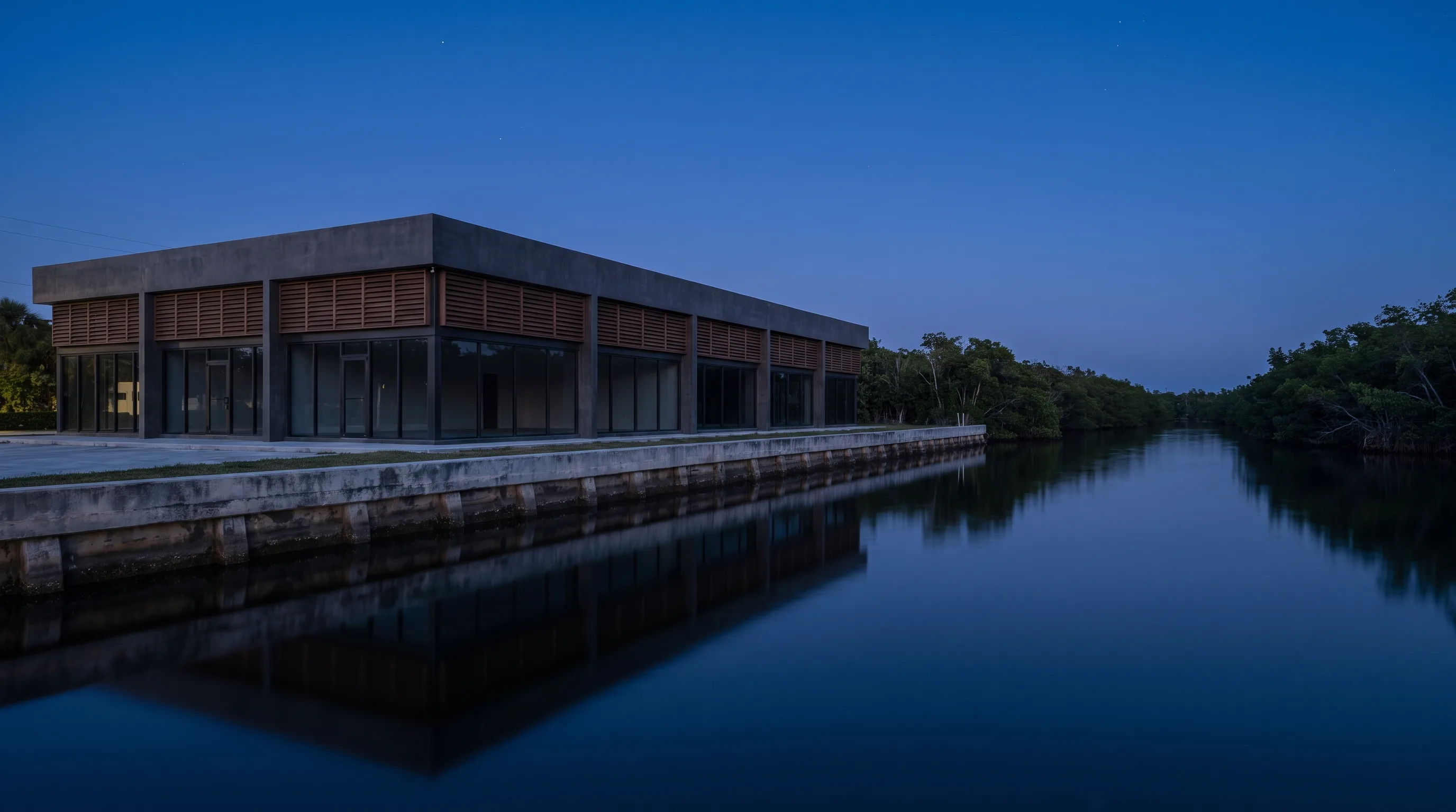 Low commercial building along a still waterway at dusk, seawall and dark water